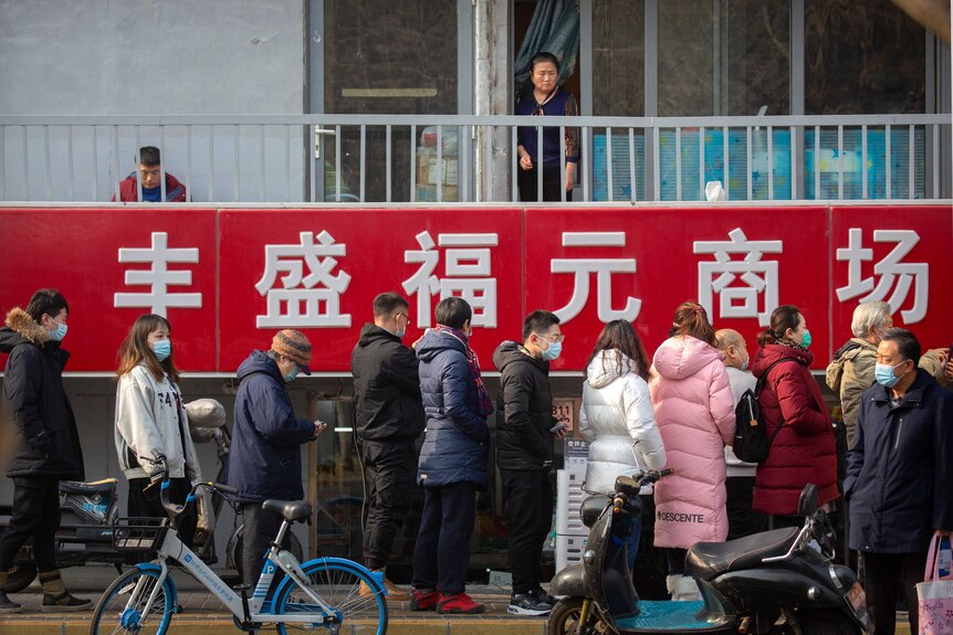 A woman looks at at people lined up for COVID testing in Beijing