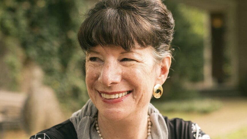 portrait of Amy Jill levine looking to the left and smiling, greenery in background