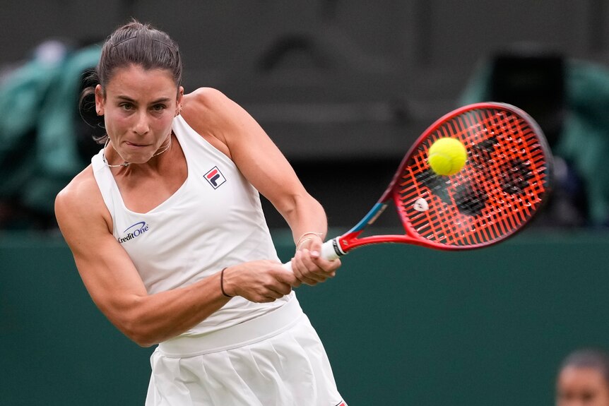 A tennis player's muscles tense as she swings the racquet through 