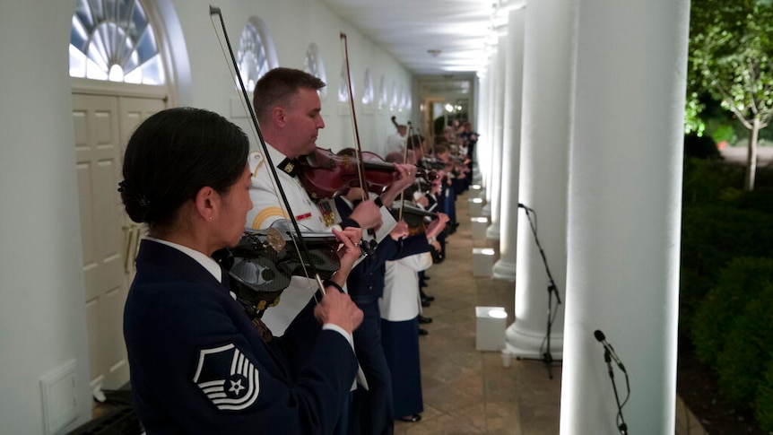 A military band, predominately violinists, play along a walkway near the Rose Garden.