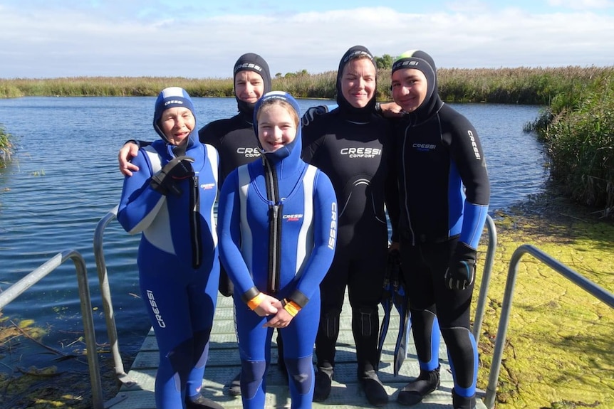 A family of five wearing head to toe wetsuits.