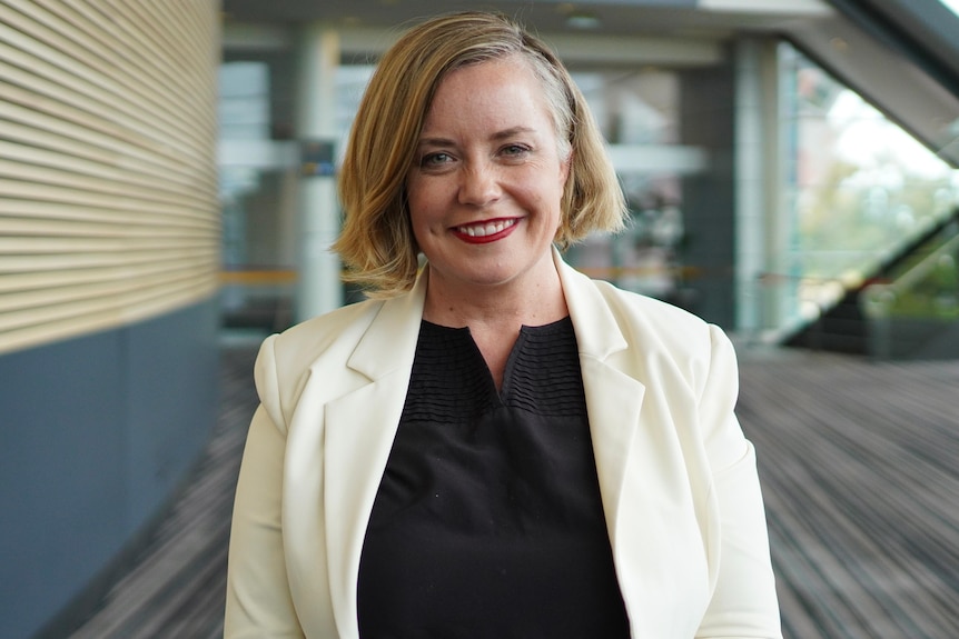 A woman with short blonde hair wearing a white blazer smiling  