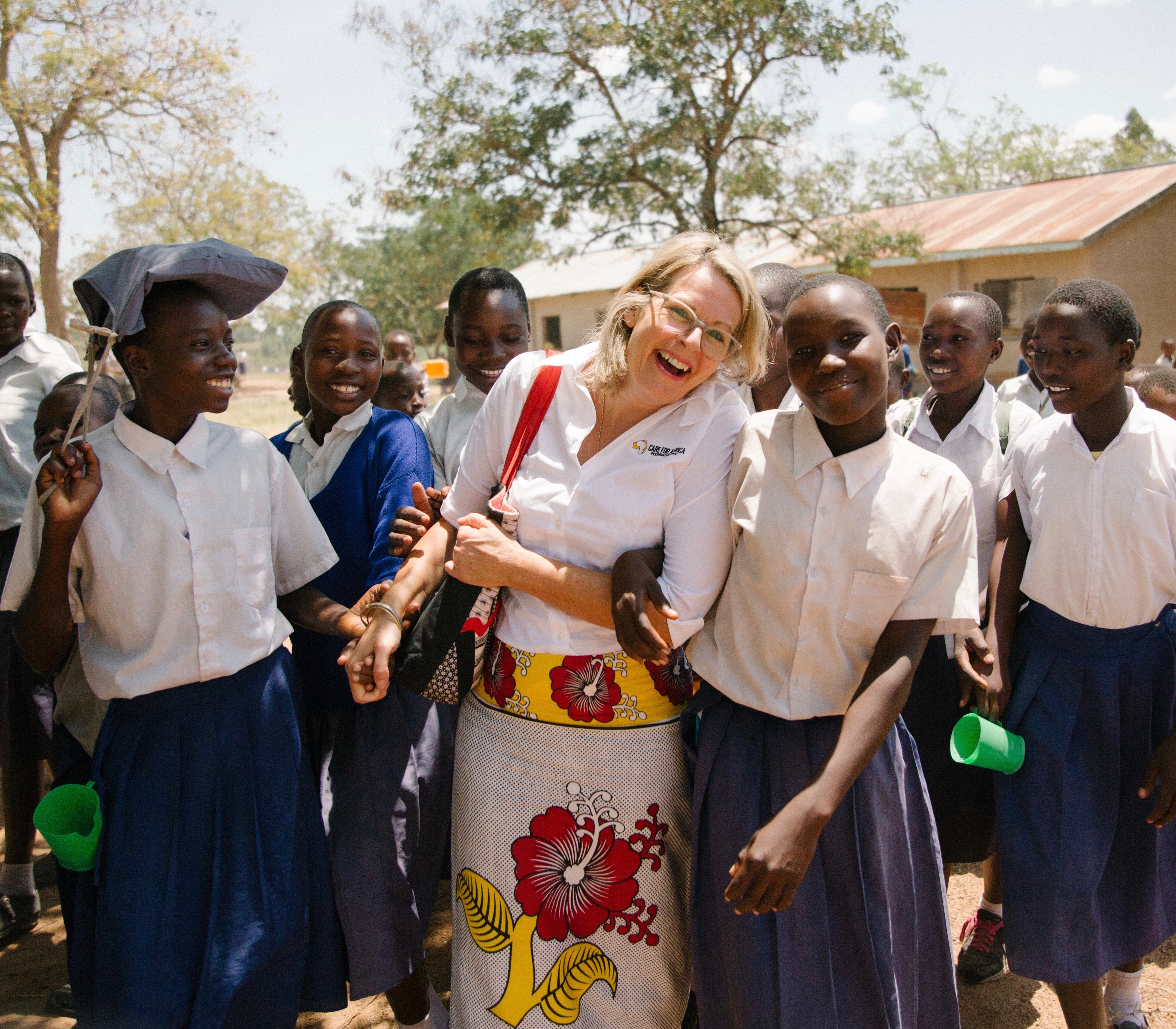 A western woman smiling and holding hands with some African school girls.