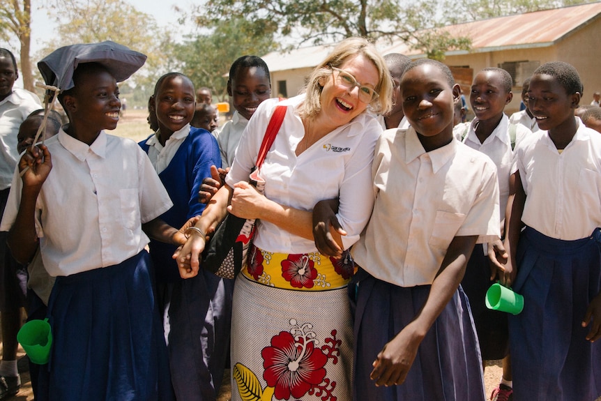 A western woman smiling and holding hands with some African school girls.