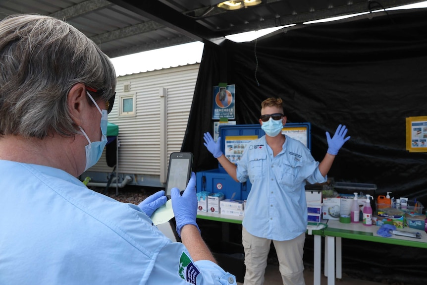 Two health workers check each other at the Howard Springs quarantine facility. One has her mobile up, both are in full PPE.