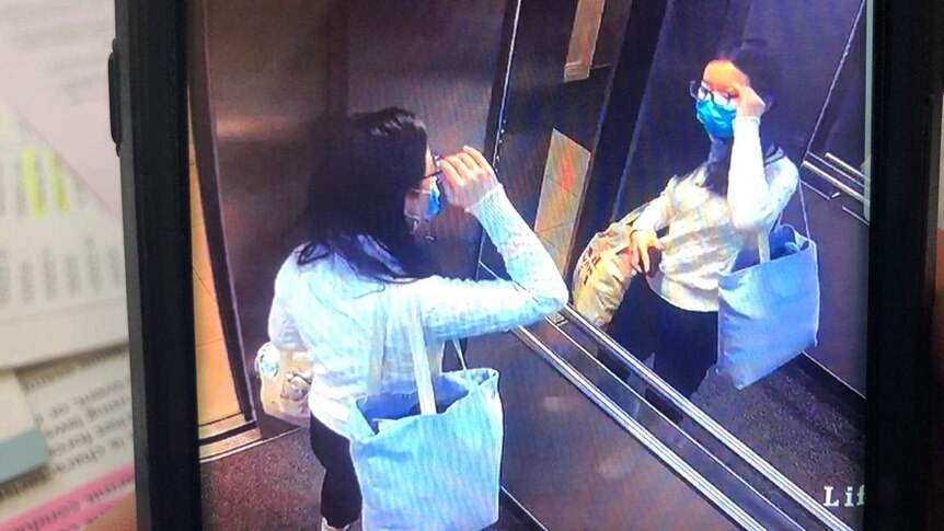 A screenshot from CCTV footage of a girl looking at herself in an elevator mirror