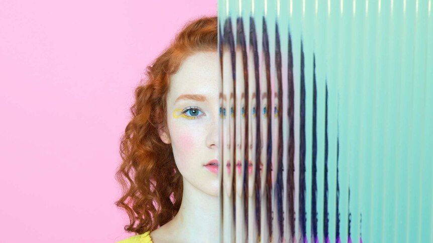 Young lady in yellow blouse with half her face blurred by wavy glass. Background colour changes from pink to blue.