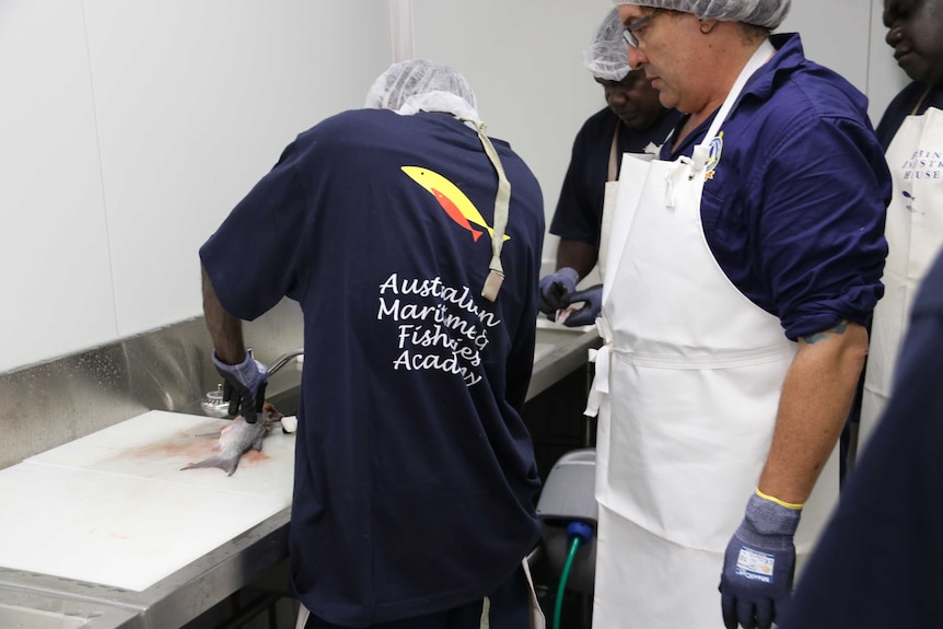 An indigenous fisherman learns how to fillet a fish as trainer Chris Francis watches on.