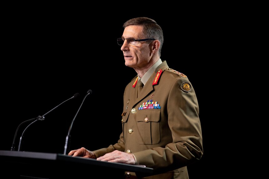 Angus Campbell in uniform speaks at a lectern against a black background
