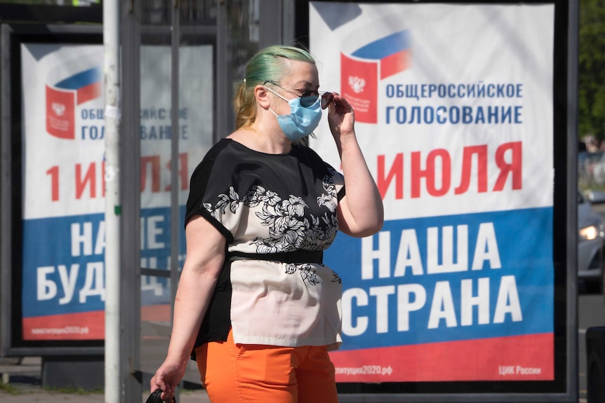 A woman, wearing a face mask to protect again coronavirus, walks past a billboard.