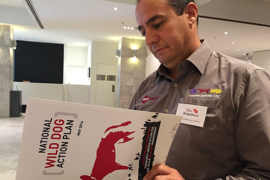 Man reads a booklet titled National Wild Dog Action Plan, Sydney meeting.