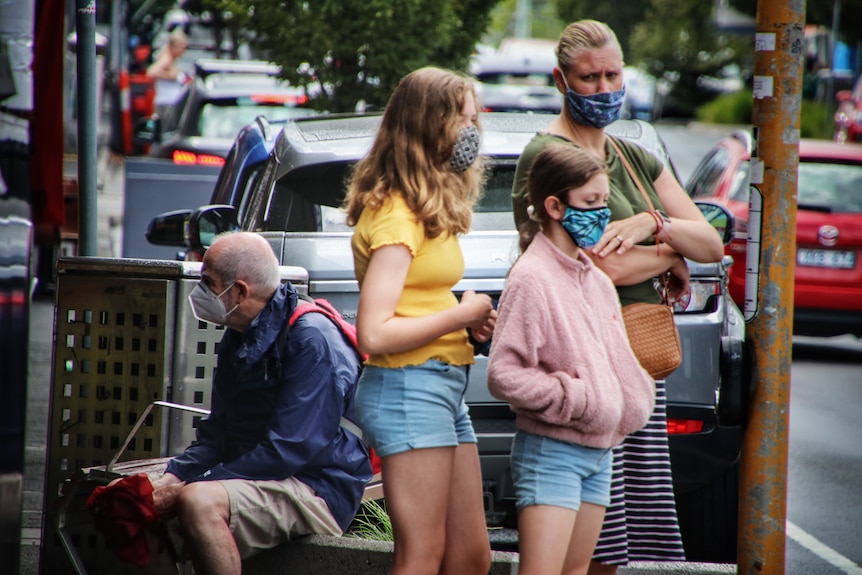 A parent and their two children, all three wearing cloth face masks, on a Melbourne street.