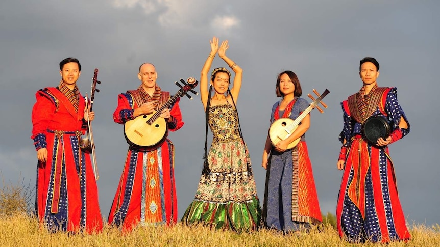 Five musicians wearing red and blue traditional Taiwanese outfits hold their instruments in front of a grey sky.