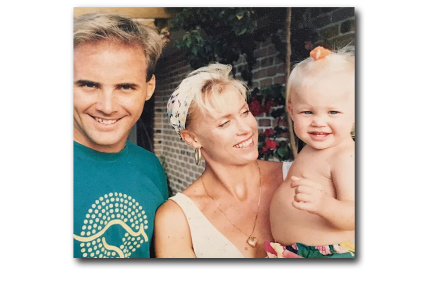 A late 1980s photograph of a man with dark blonde hair and a woman with blonde hair who is holding a toddler girl, smiling