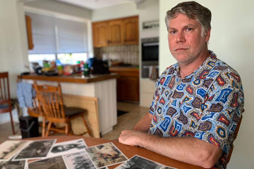 John Patten sits at a table in his kitchen, covered in historical photos of his ancestor John Patten.