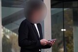 Image of a person outside court in Perth. Their face is blurred and they are wearing a black suit jacket with a white shirt.