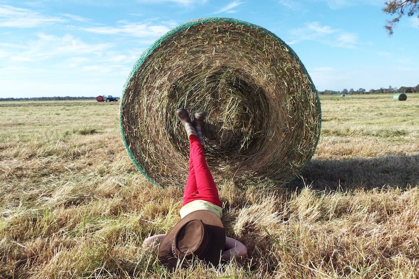 A woman lies on the ground, feet on a hay bale.