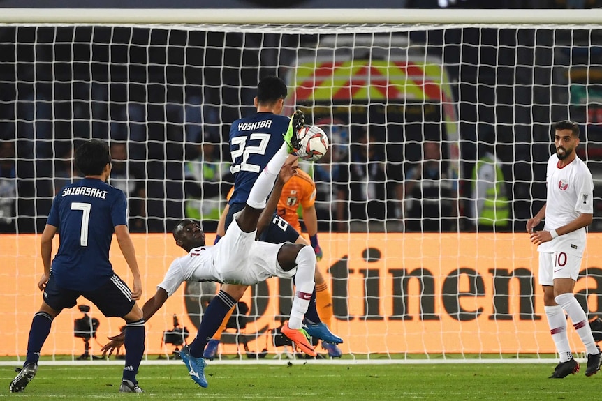 A Qatari forward wearing a white kit makes an overhead kick as a Japanese defender turns his back