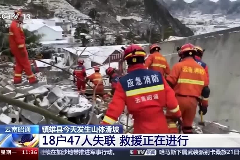 A group of people wearing red jumpsuits with chinese characters climb over large bits of rubble.