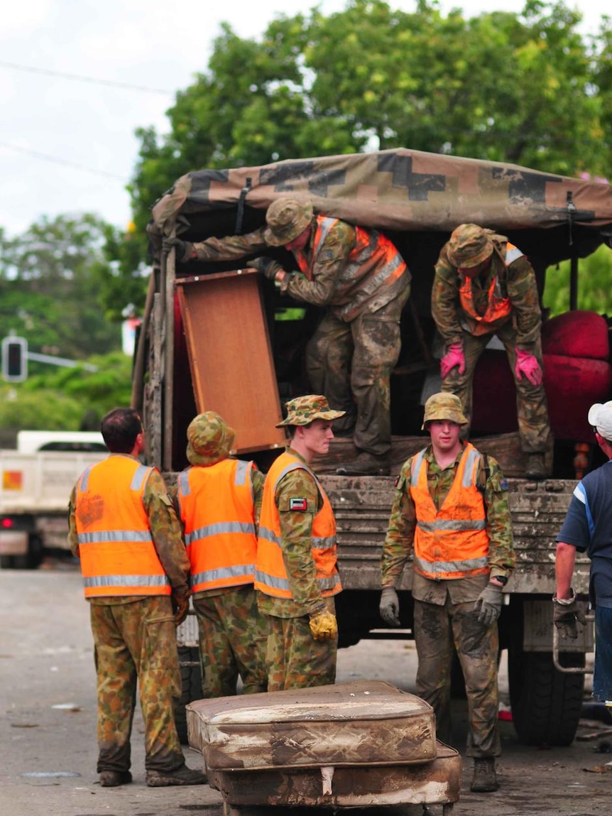 Defence personnel load ruined furniture into their vehicle after a flood inundated the Brisbane suburb of Fairfield.