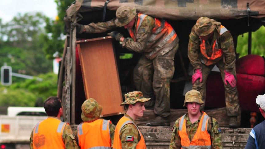 Defence personnel load ruined furniture into their vehicle after a flood inundated the Brisbane suburb of Fairfield.