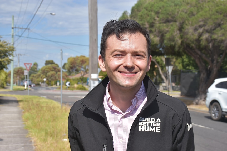 A man smiling at the camera with a residential street in the background.