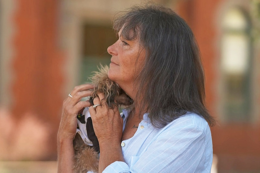 A woman cuddles a small dog.