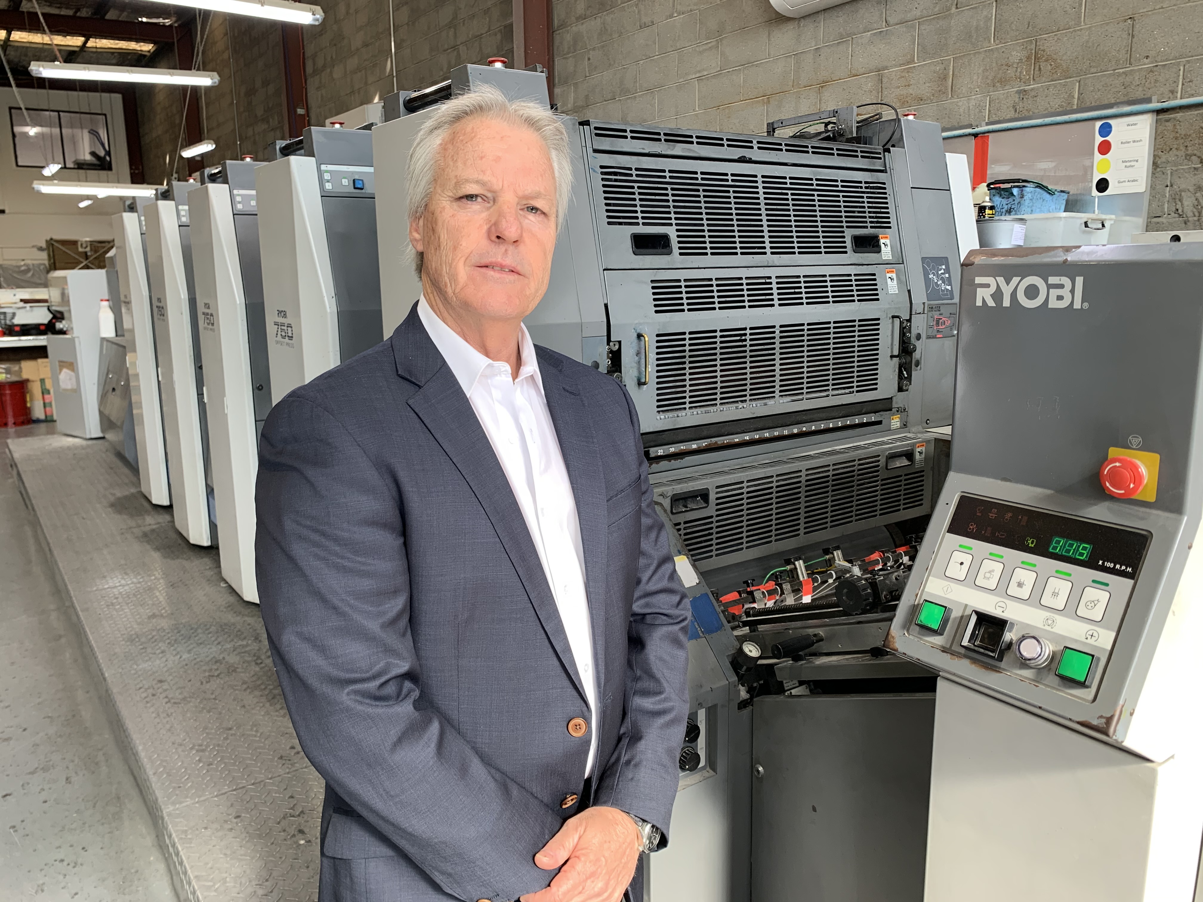 Walter Kuhn, wearing a suit jacket, stands in front of printing machinery.