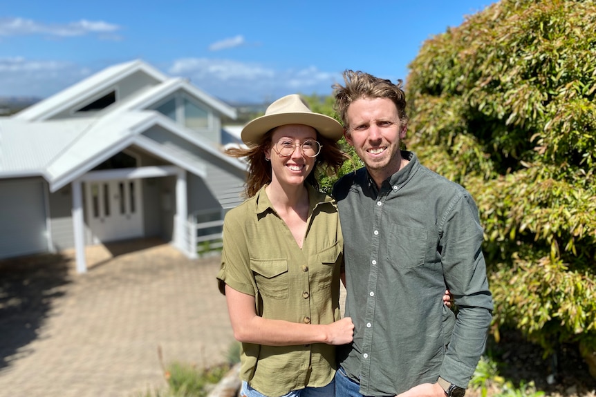 Holly and David Ramsay stand with arms around each other with their home in the background.