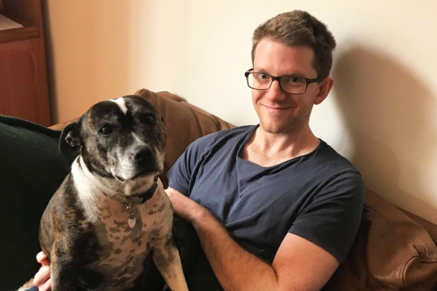 Writer and journalist Alex McKinnon sitting on a couch with his dog.