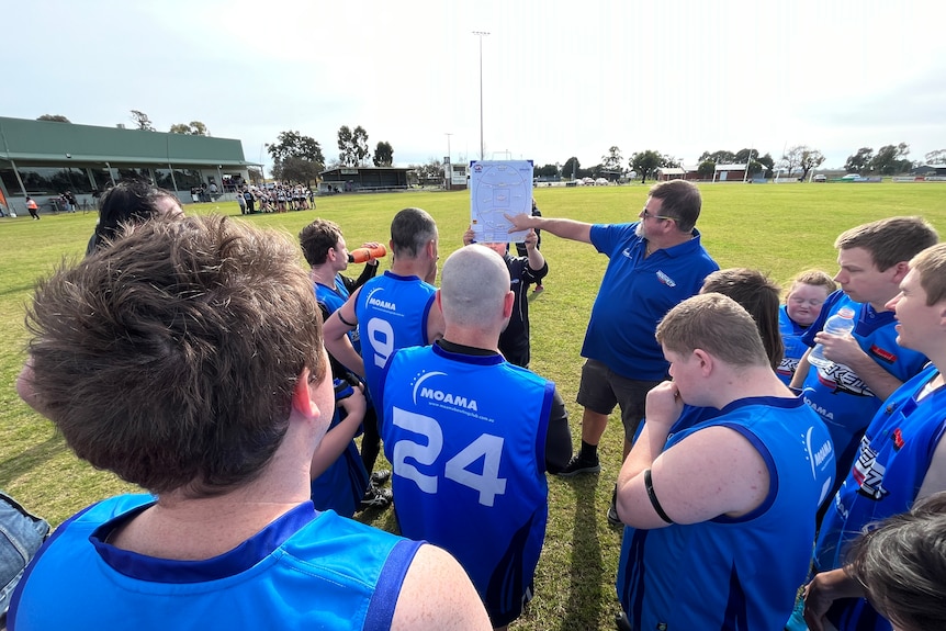 Graeme is pointing at a diagram of the footy oval, surrounded by the Rockets team at halftime.