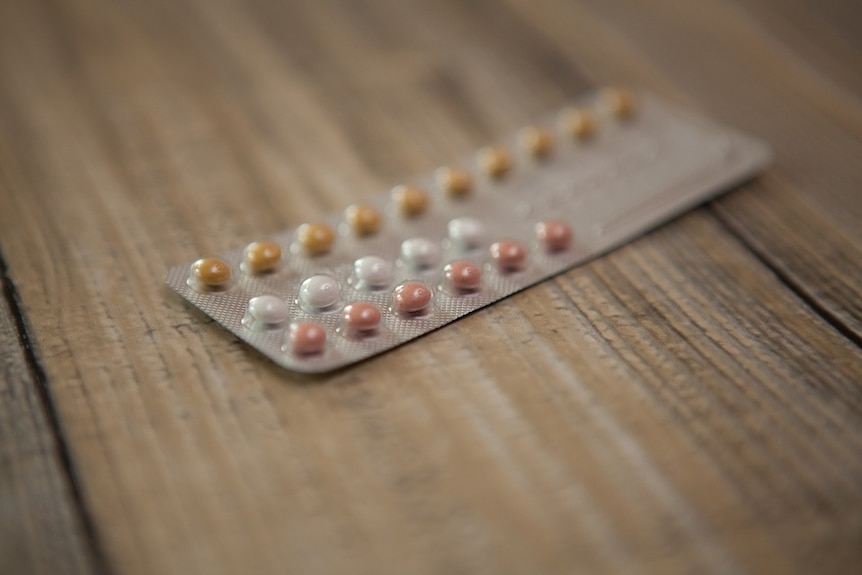 A full packet of contraceptive pills on a wooden board.