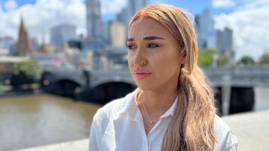 A young woman with a white shirt and dyed blonde hair looks to the left of frame.