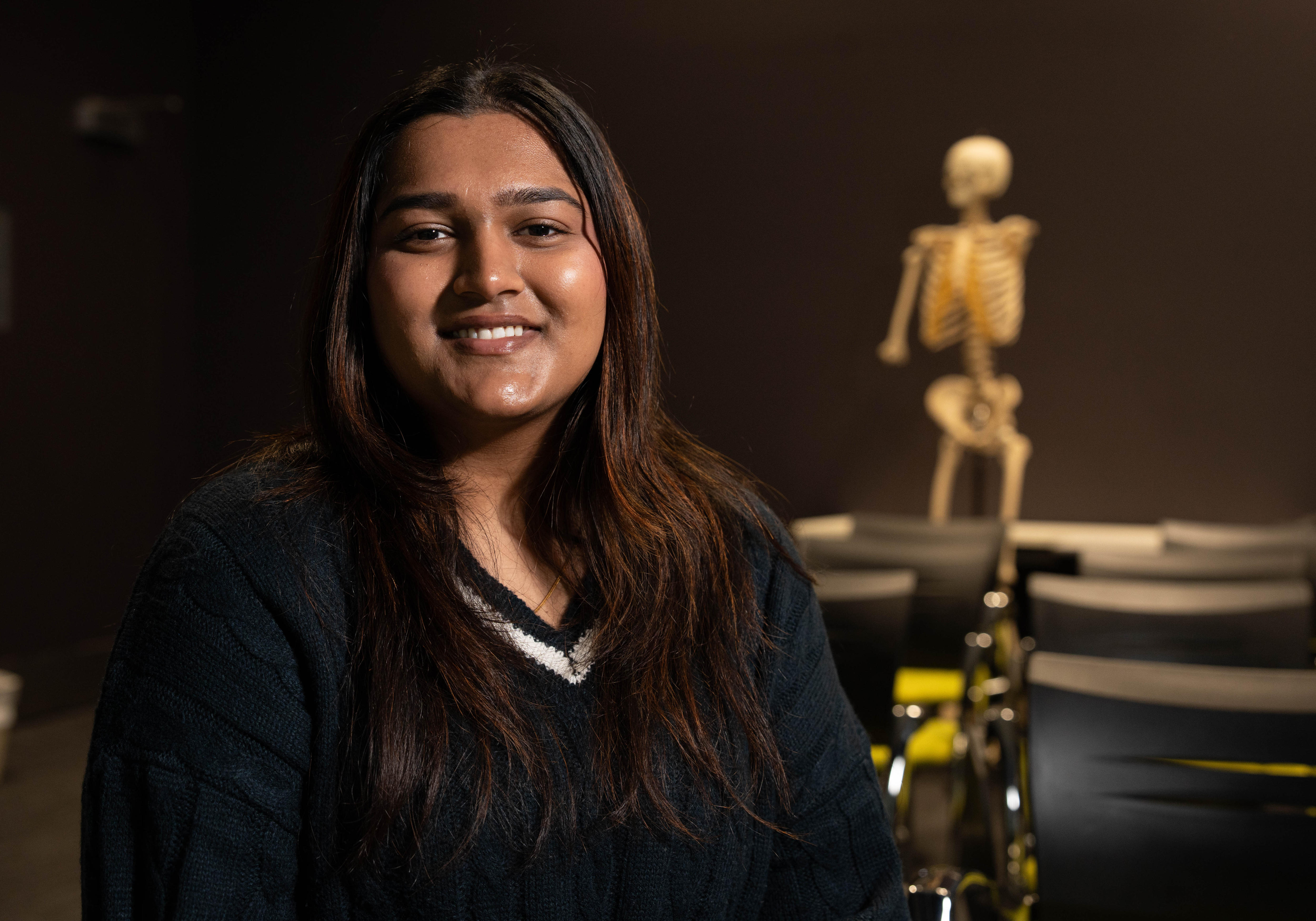 A woman smiles for the camera, with a skeleton pictured in the background.