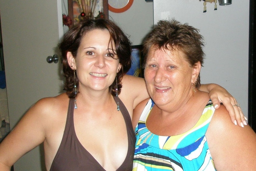 a young woman smiles standing with her arm around a woman with short hair