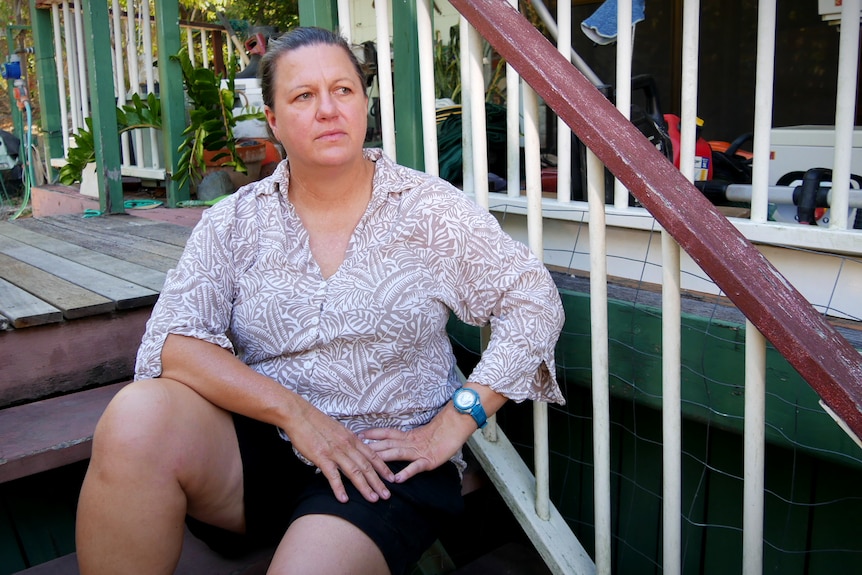 A woman sits on the stairs outside a house and stares into the distance