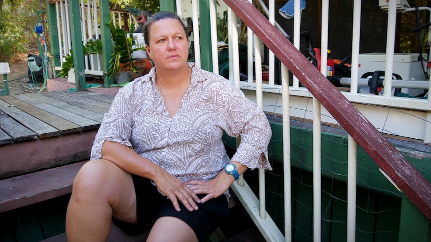 A woman sits on the stairs outside a house and stares into the distance