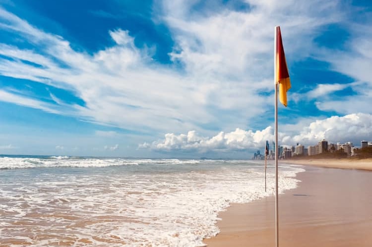 A beach with no people showing a lifesaving pole with high-rise buildings in the distance