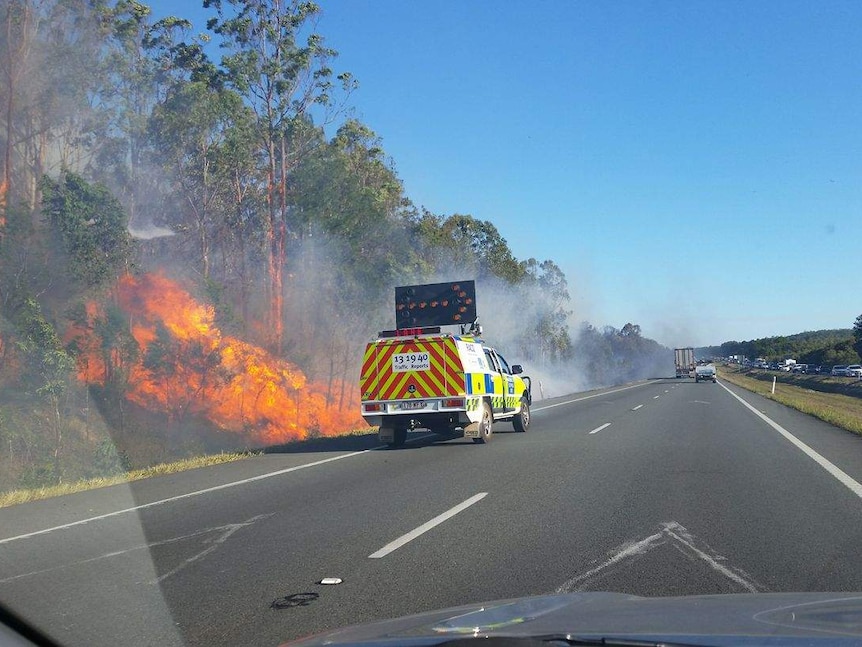 fire burns alongside highway with fire truck trying to control it