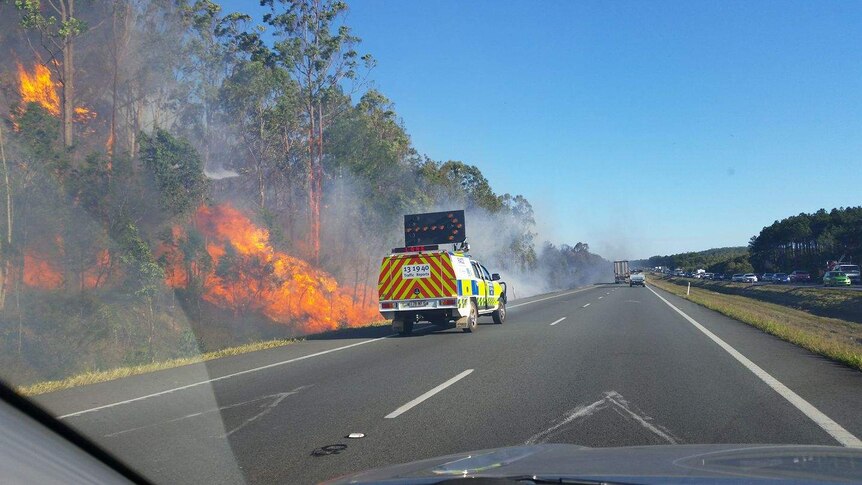 fire burns alongside highway with fire truck trying to control it