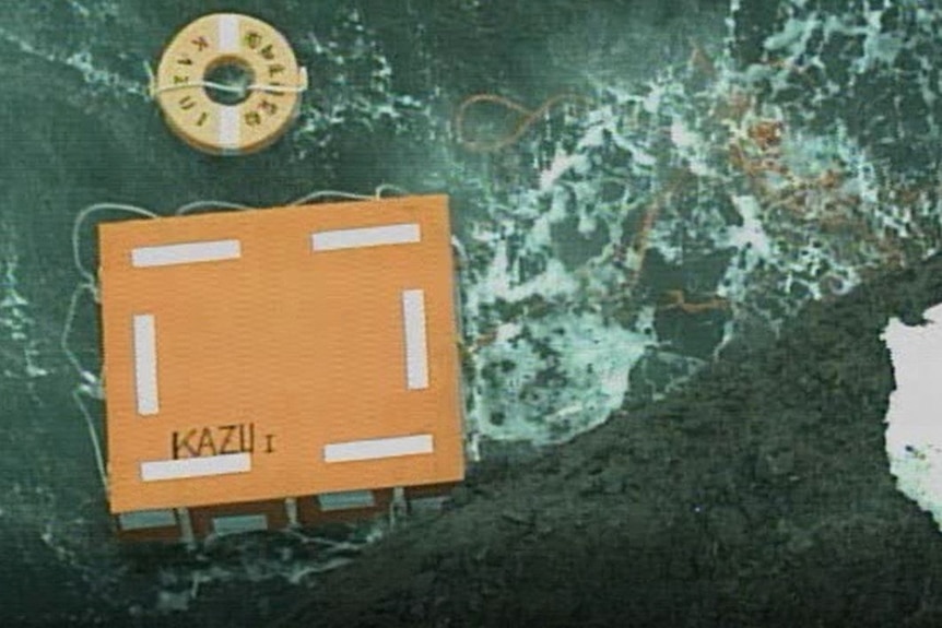 A bird's eye view of swimming equipment, a box labeled 'Kazoo 1' and some ropes floating in the water near the rocks.