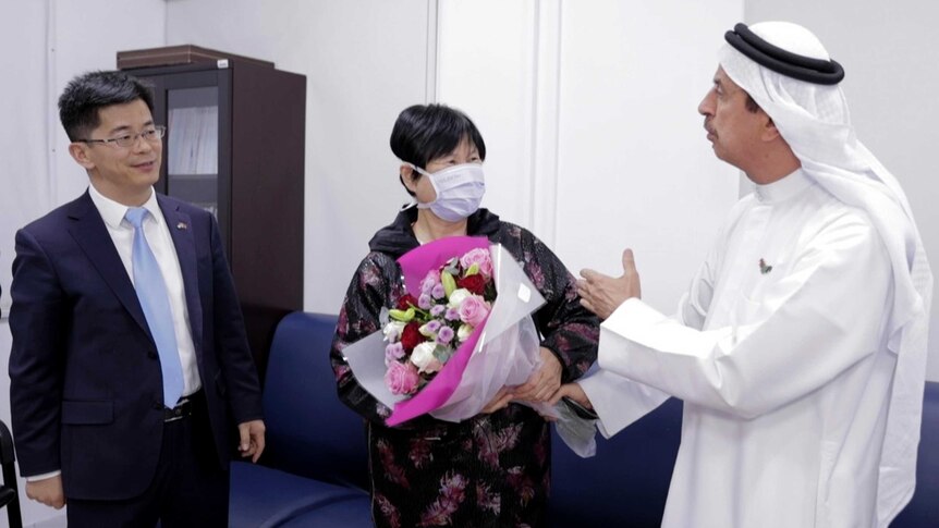 A Chinese women wearing a mask receives a bouquet of flowers from a doctor wearing a Middle East head dressing.
