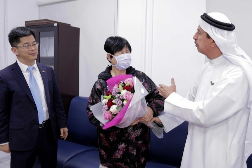 A Chinese women wearing a mask receives a bouquet of flowers from a doctor wearing a Middle East head dressing.