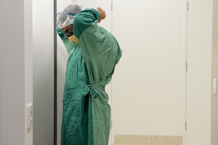 a hospital worker wearing a head covering, hospital tunic standing while putting on a mask