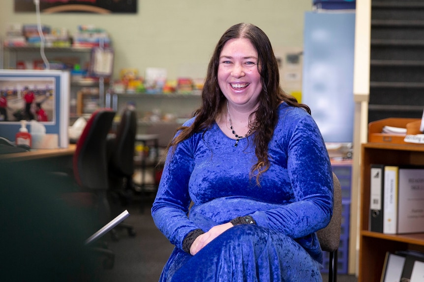 A woman in a blue dress sits and smiles.