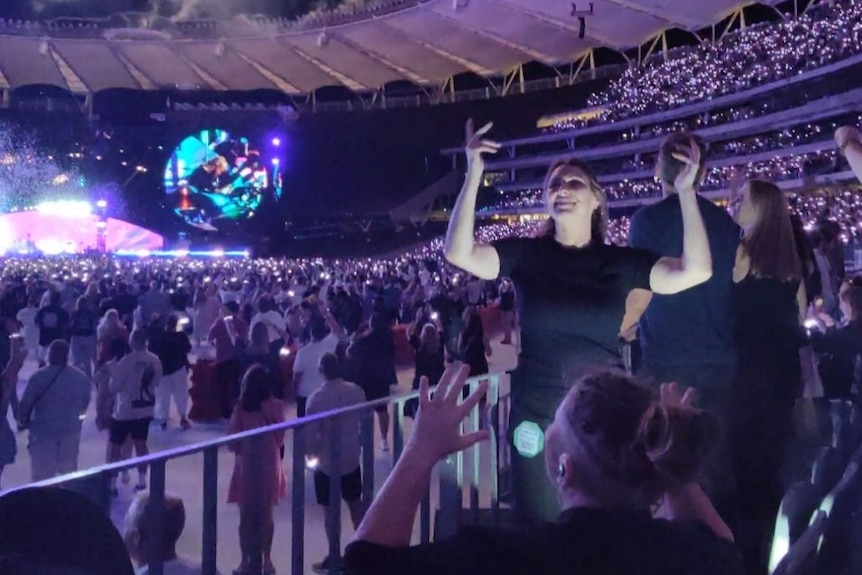 An Auslan interpreter at the Coldplay concert gestures as fireworks explode in the background.