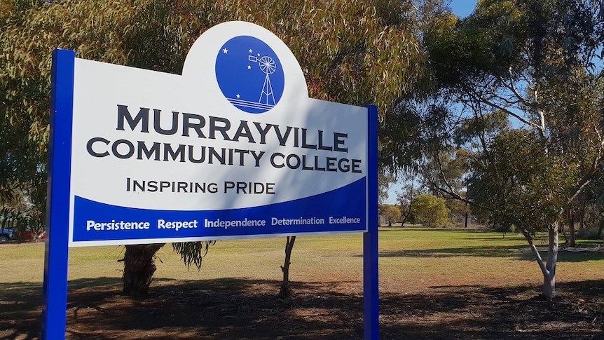 A white sign with blue edges stands on the side of an oval. There are trees around it.