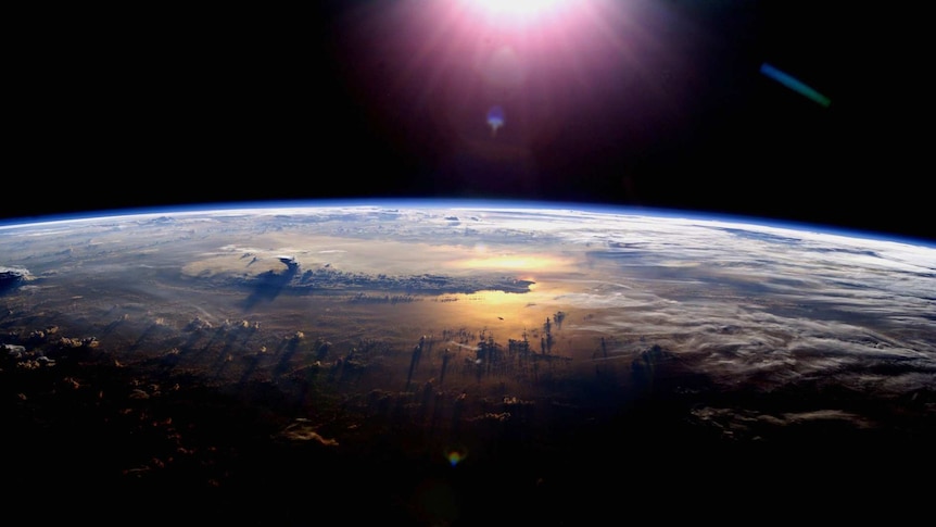 The curvature of the Earth seen from space with the Sun glinting off the ocean at sunset with a thunderstorm.