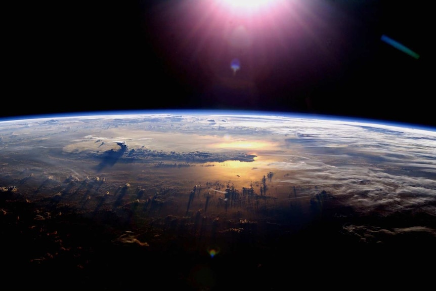 The curvature of the Earth seen from space with the Sun glinting off the ocean at sunset with a thunderstorm.