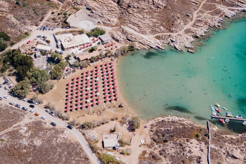 A photograph, taken from above, of dozens of umbrellas and sunlounges on a sandy beach.